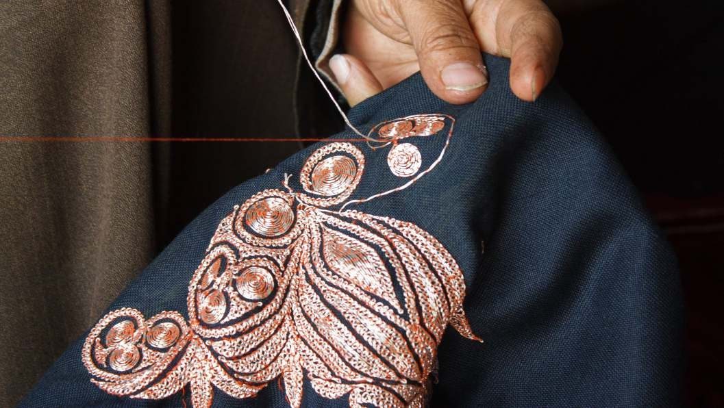 An artisan's hands working metallic thread into a flower on dark cotton