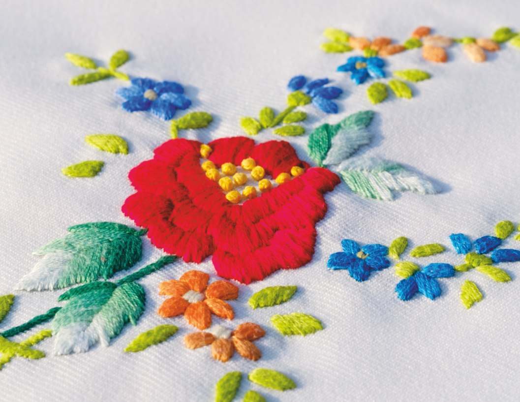 A red flower worked in close hand embroidery surrounded by leaves